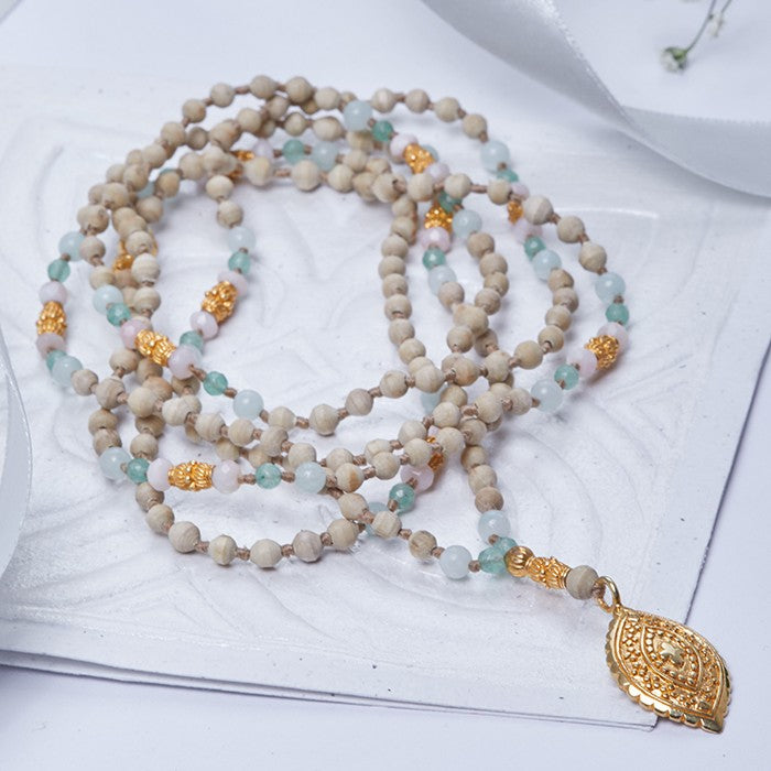 Shivaloka Talusi Devi handknotted mala created with 216 beads ( 2 x 108) in an assortment of tulsi wood beads, amazonite, and pink opal; strung on silk with petal-shaped, 22k gold vermeil pendant.  Mala length: 114 cm / 45” , Sanskrit meaning: Tulsi goddess.