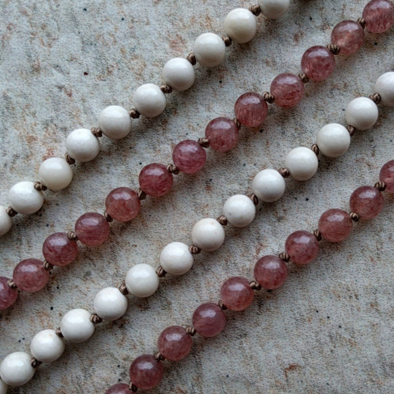 The ZenStones Atma-Prema mala with 108 natural 6 mm Riverstone and Strawberry Quartz beads.  Each bead is lovingly hand knotted on a garland of caramel colored brown silk cord, and accented with a Strawberry Quartz guru bead above a handmade cream colored cotton tassel. Chain length: approximately 33" or 84 cm. 