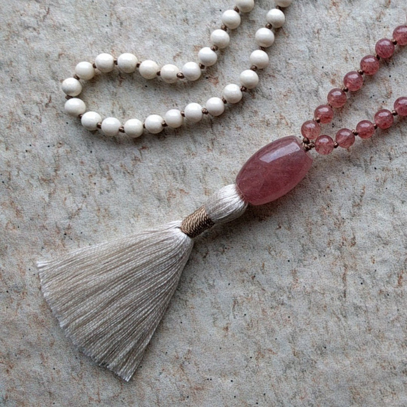 The ZenStones Atma-Prema mala with 108 natural 6 mm Riverstone and Strawberry Quartz beads.  Each bead is lovingly hand knotted on a garland of caramel colored brown silk cord, and accented with a Strawberry Quartz guru bead above a handmade cream colored cotton tassel. Chain length: approximately 33" or 84 cm. 